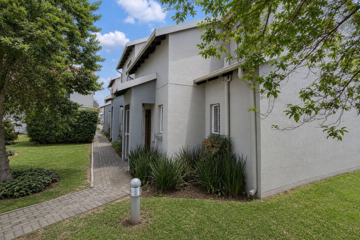 Exterior view of the townhouse complex featuring paved walkways, manicured lawns, and established garden landscaping along the building facade.