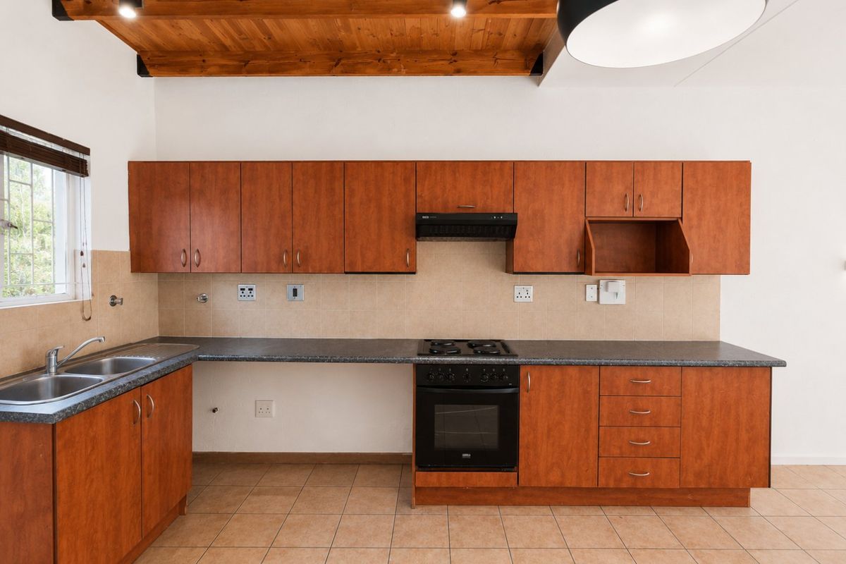 A functional kitchen featuring wooden cabinetry, a built-in oven with gas hob, extractor fan, double sink, and exposed timber ceiling beams.