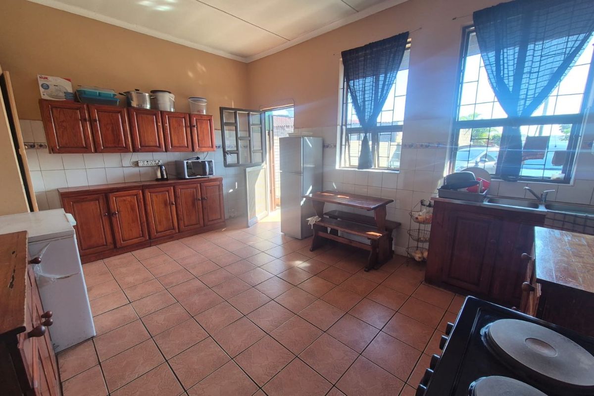 A spacious kitchen featuring wooden cabinetry, tiled flooring, and a tiled splashback, offering functional storage and preparation space with natural light.