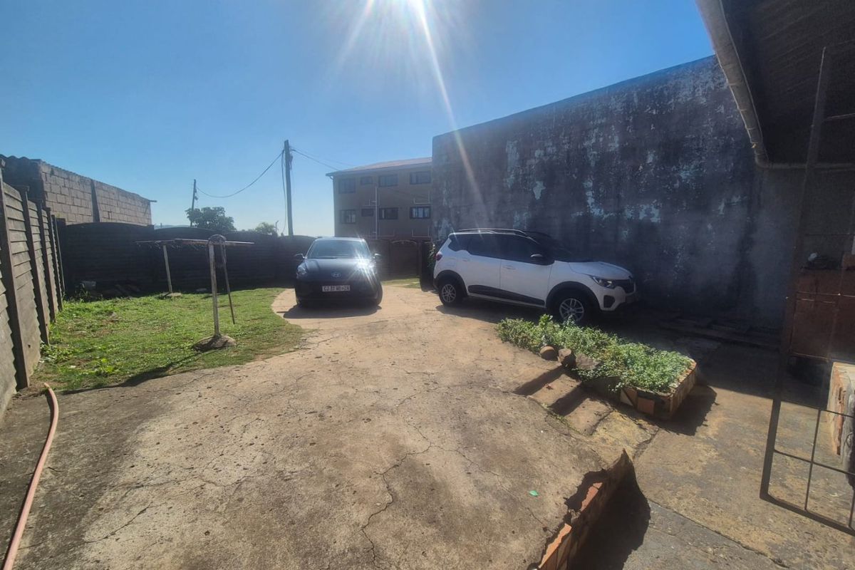 Rear exterior area featuring a concrete driveway, boundary walls, and a raised garden bed, showing signs of significant weathering and surface cracking.