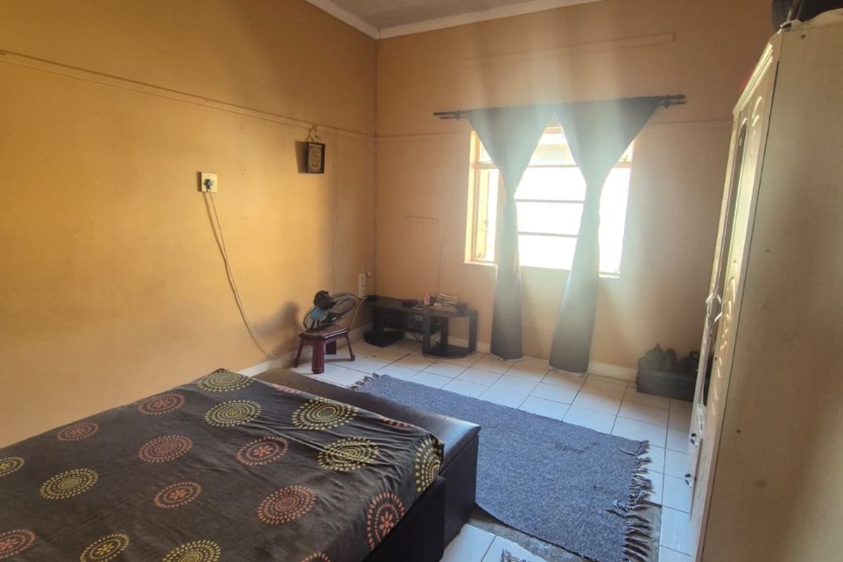 A bedroom featuring tiled flooring and natural light from a single window. The space requires cosmetic updates to the wall and ceiling finishes.