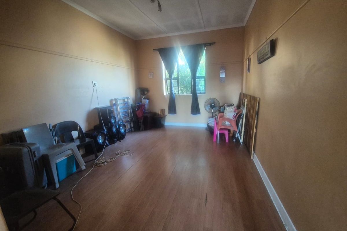 A living room featuring laminate flooring and a picture rail, currently used for storage. The space requires cosmetic updates to improve its appeal.