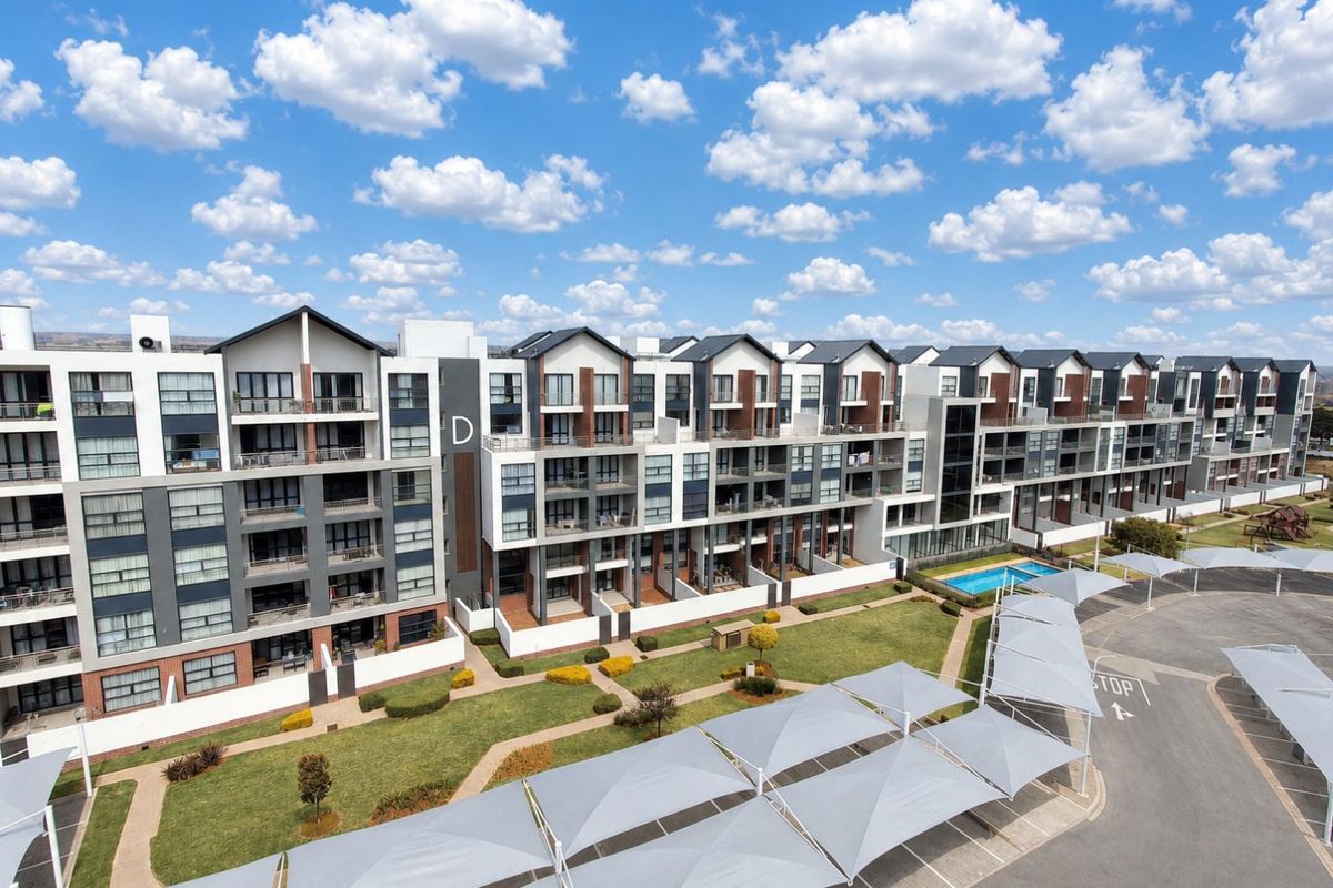 Aerial view of a modern apartment complex featuring landscaped grounds, a swimming pool, and covered parking bays.