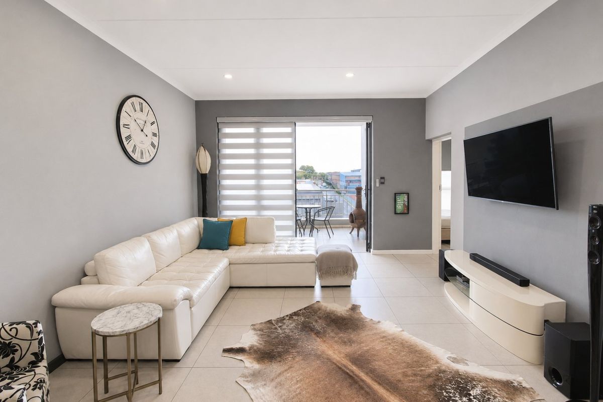 Modern living room featuring neutral grey walls, tiled flooring, recessed lighting, and direct access to a private balcony through sliding glass doors.