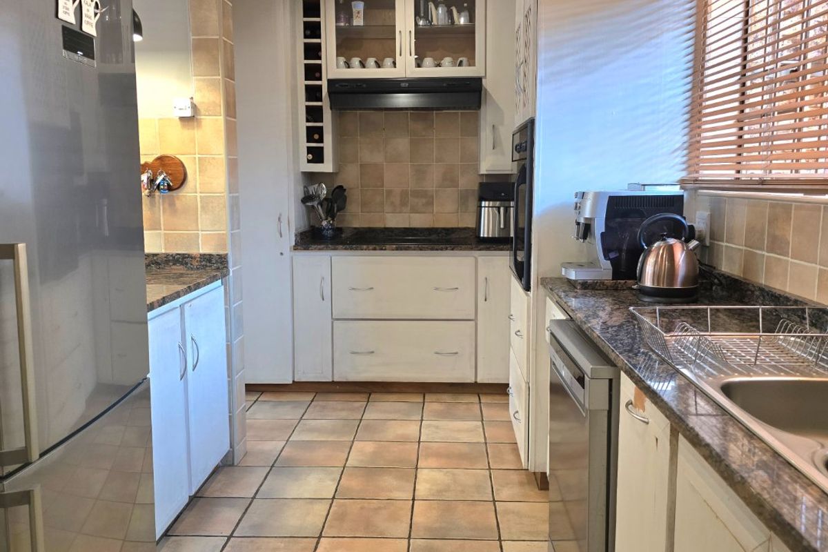 A functional galley-style kitchen featuring granite countertops, tiled backsplash, built-in oven, and ample cabinetry with integrated wine storage.