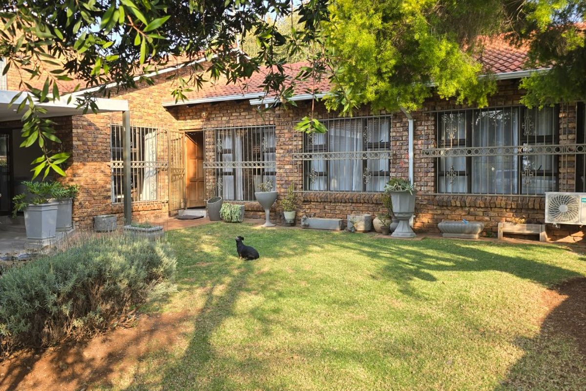 Rear view of a face brick townhouse featuring a well-maintained lawn, security bars on windows, and an integrated air conditioning unit.