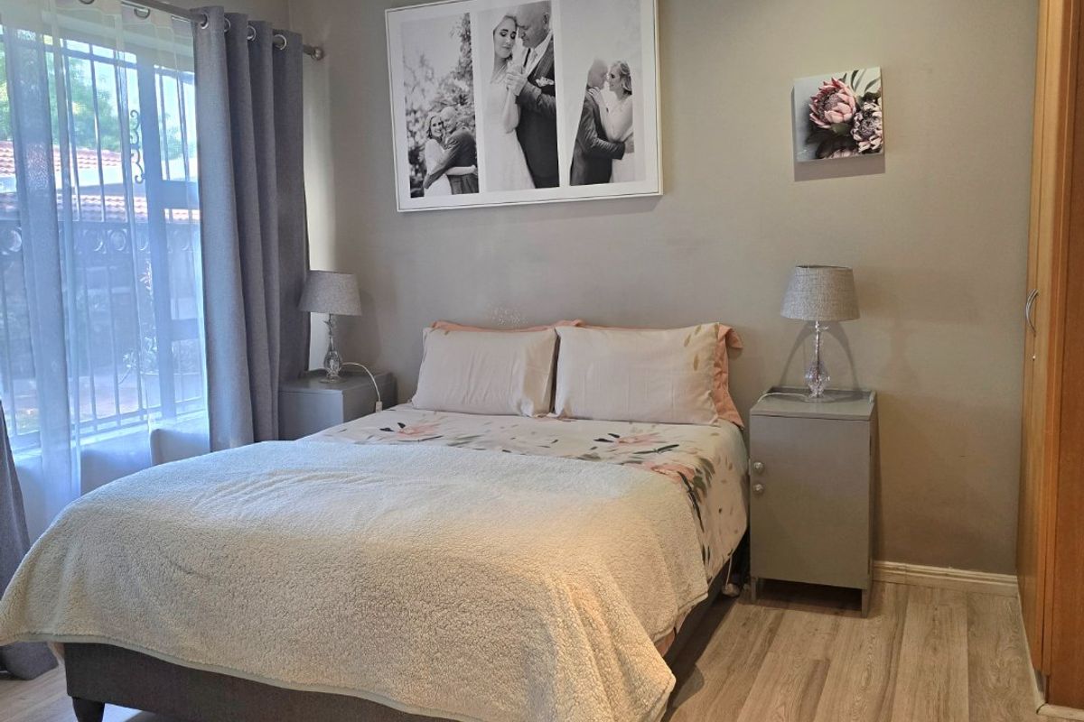 A well-maintained bedroom featuring light-toned laminate flooring, recessed ceiling lighting, and a built-in wardrobe, with security bars installed on the window.