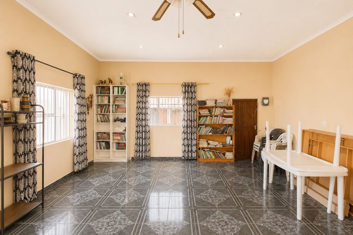 Spacious living area featuring tiled flooring, recessed ceiling lighting, a central ceiling fan, and security-barred windows, offering a functional and well-lit living space.