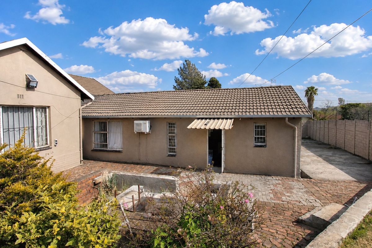 Rear exterior view of the property featuring a tiled roof, brick paved patio area, and security features on windows.