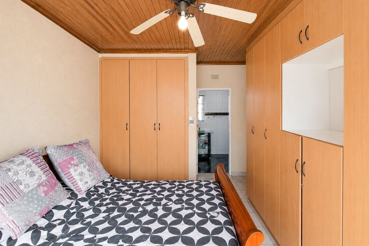 A bedroom featuring extensive built-in cabinetry, a timber-clad ceiling with a central fan, and direct access to an en-suite bathroom.