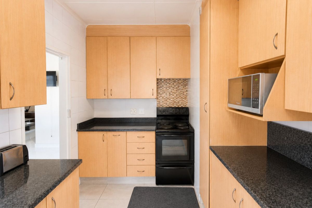 A functional kitchen featuring light wood-tone cabinetry, dark granite countertops, a built-in electric stove, and tiled flooring.