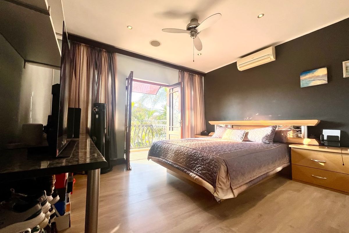 Spacious bedroom featuring laminate flooring, a ceiling fan, split-system air conditioning, and direct access to a private balcony through double doors.