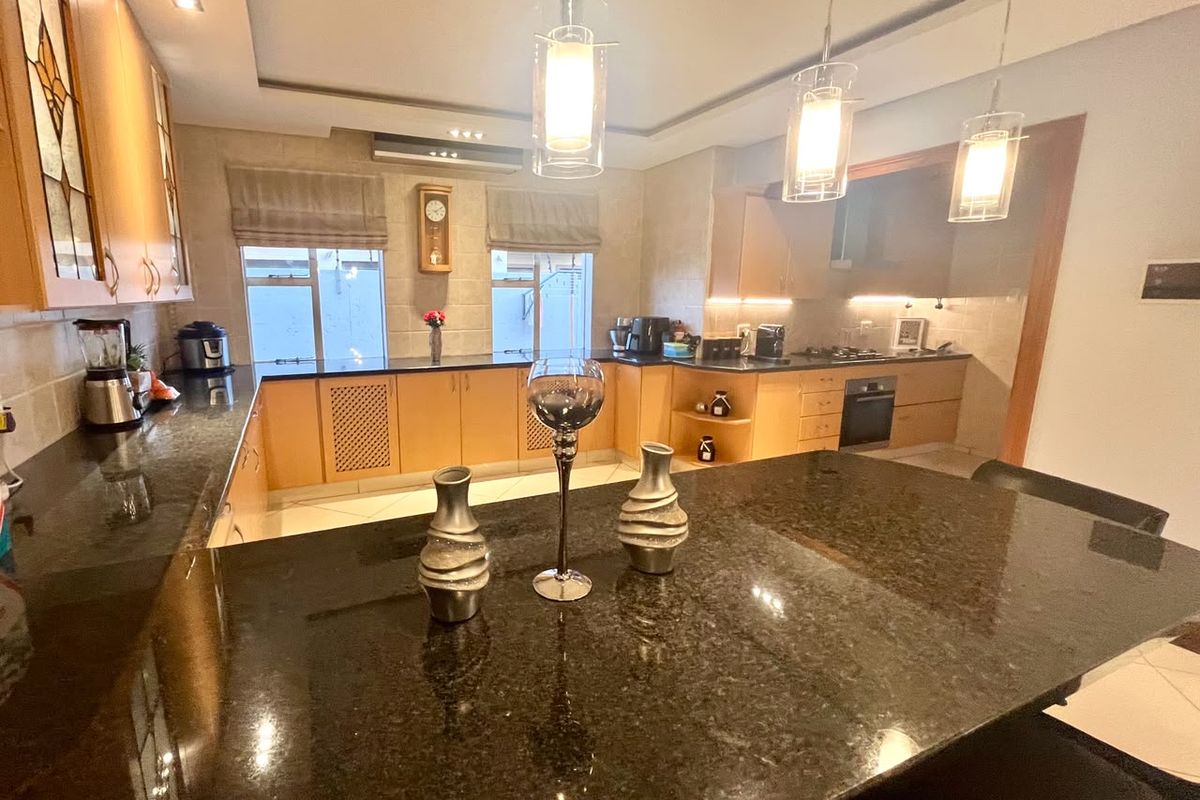 Spacious kitchen featuring granite countertops, built-in oven, hob, extractor fan, and modern pendant lighting, offering a functional and well-lit culinary workspace.