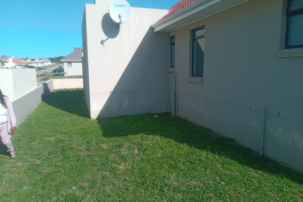 Rear exterior view of the house showing the lawn, plastered walls, tiled roof, and a satellite dish installation.