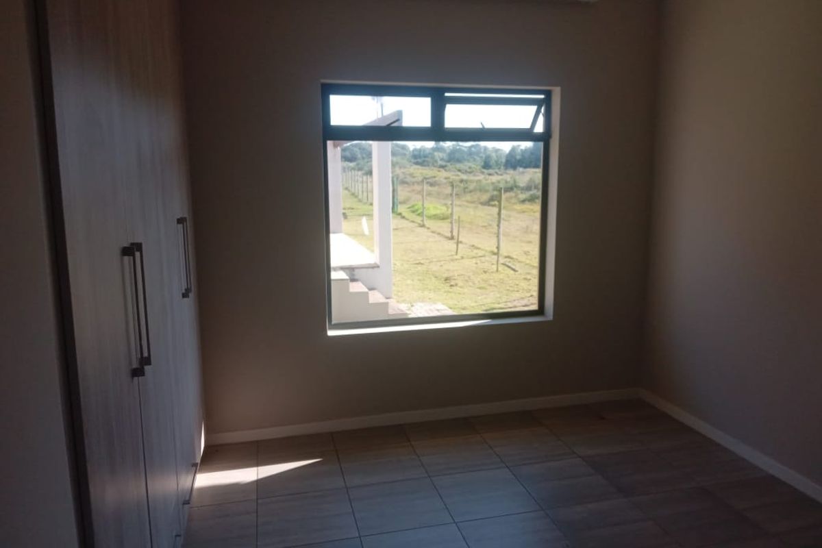 A bright, empty bedroom featuring modern tiled flooring and built-in cupboards, offering a clean space with a view of the surrounding landscape.