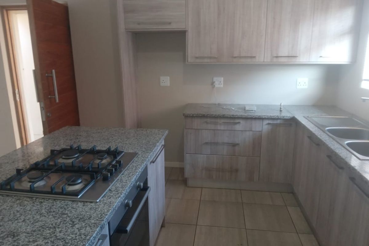 Modern kitchen featuring light wood-finish cabinetry, granite countertops, a gas hob, built-in oven, and double bowl sink with tiled flooring.