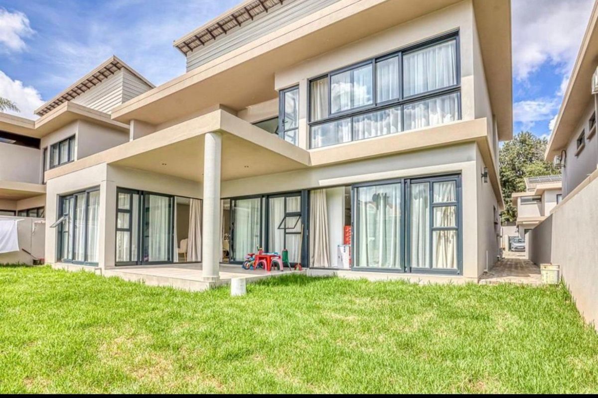 Rear view of a modern two-story house featuring a covered patio, large sliding glass doors, and a well-maintained lawn.