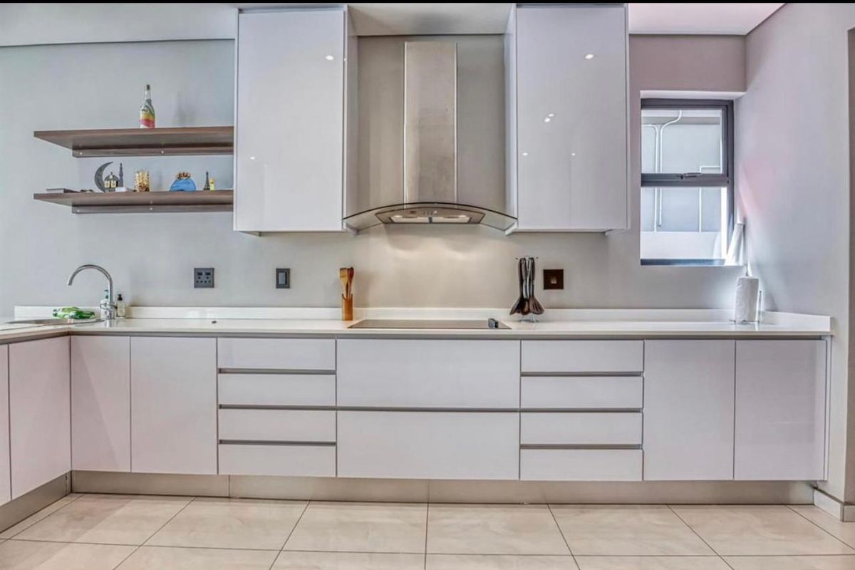 Modern kitchen featuring sleek white gloss cabinetry, stone countertops, a stainless steel extractor fan, and integrated hob with clean tiled flooring.