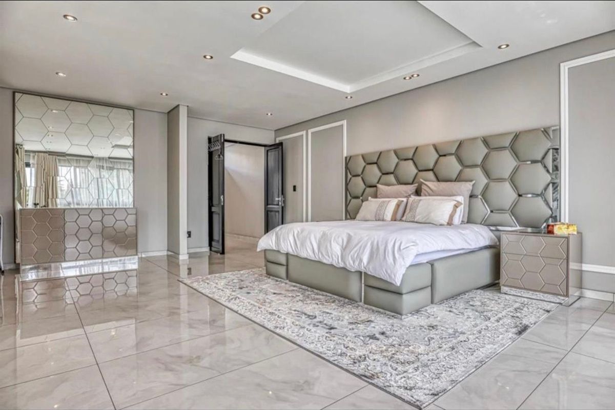A spacious, modern bedroom featuring high-gloss porcelain floor tiles, a coffered ceiling with recessed lighting, and a custom integrated headboard.