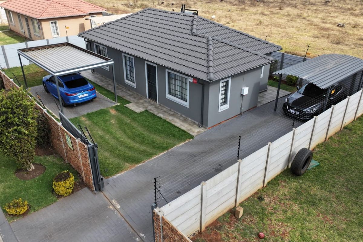 Aerial view of a well-maintained detached house featuring a tiled roof, paved driveway, dual carports, and secure perimeter walling with electric fencing.