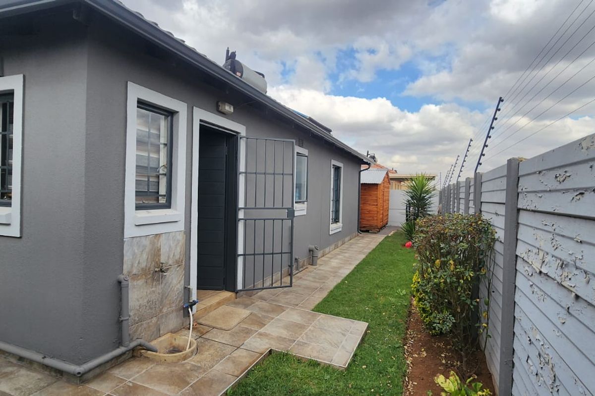 Rear exterior view of the property featuring a tiled patio area, security gate, and perimeter wall with electric fencing.
