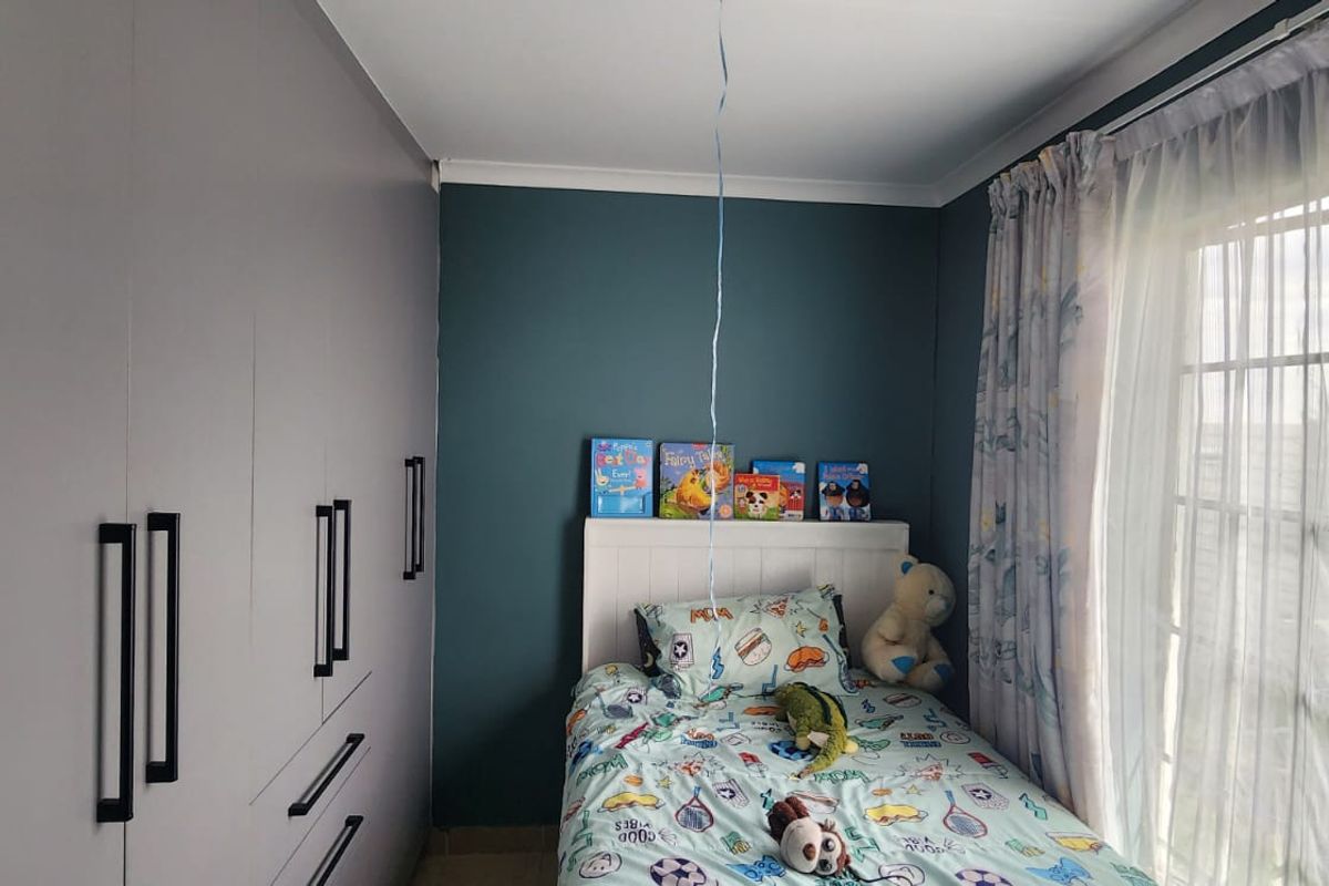 A well-maintained bedroom featuring modern built-in cupboards with sleek black handles and access to a patio or garden through a sliding door.