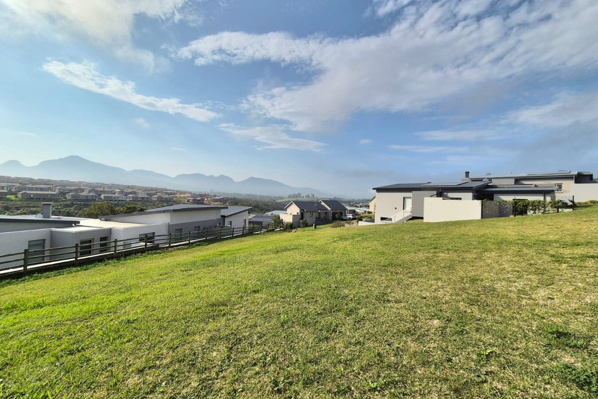 A wide-angle view of a sloped residential plot featuring manicured grass, timber fencing, and scenic mountain views in a developed estate setting.