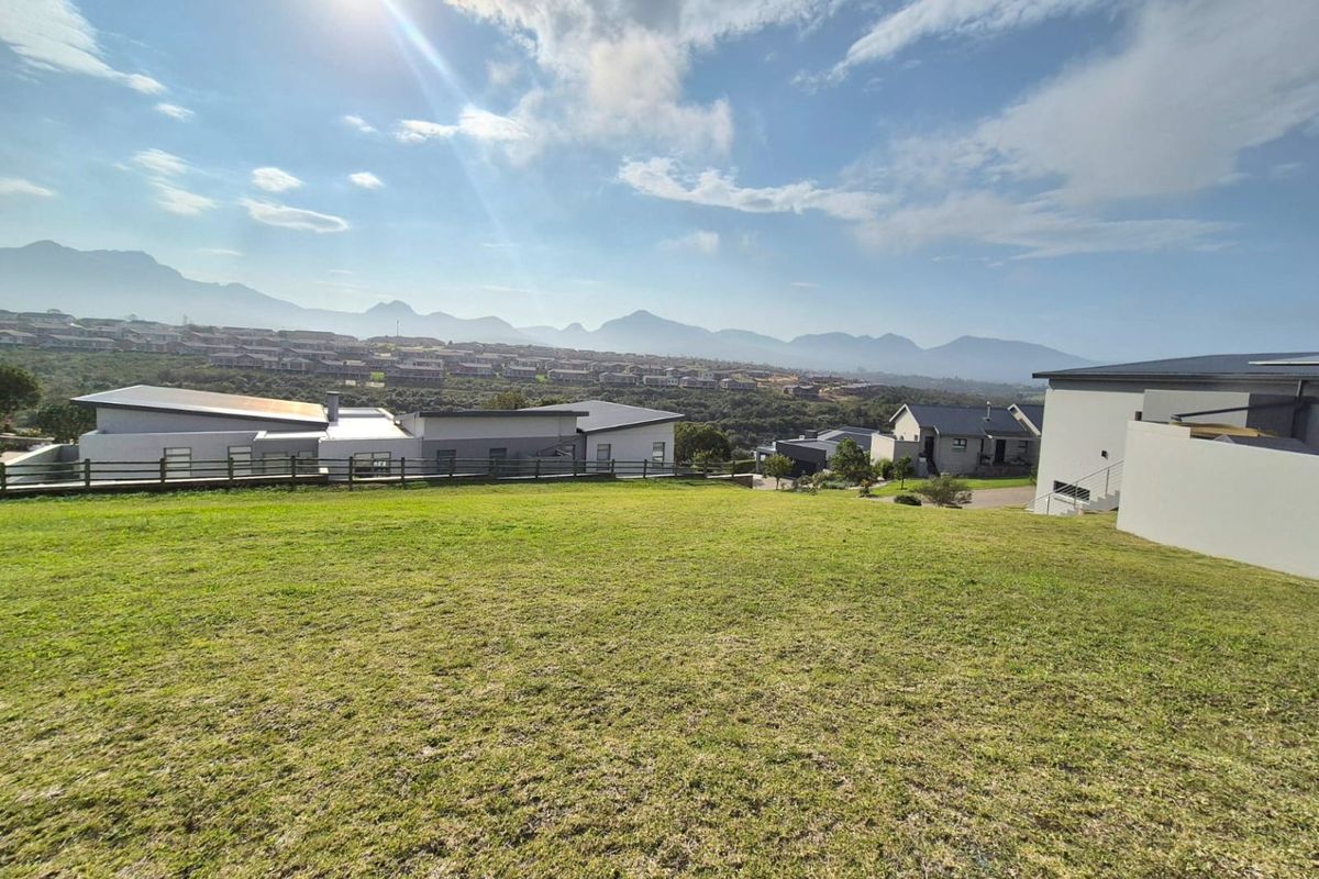 A wide-angle view of a residential vacant land plot featuring a grass lawn, timber fencing, and scenic mountain views in the background.