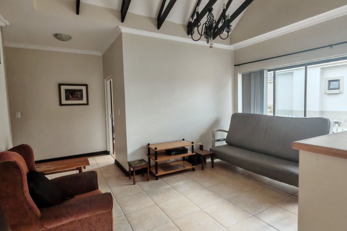 A living room featuring exposed timber ceiling beams, ceramic floor tiles, and a sliding glass door providing natural light.