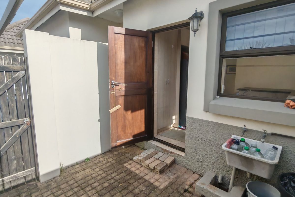 Rear exterior view showing a timber door, external utility sink, and paved patio area with timber fencing.