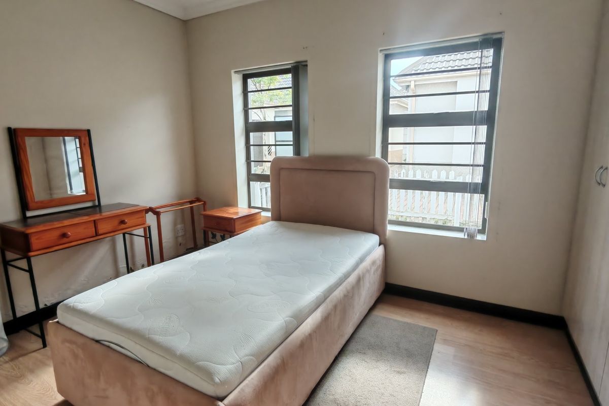 A well-lit bedroom featuring laminate flooring, built-in cupboards, and aluminium windows with security bars, offering a clean and functional living space.