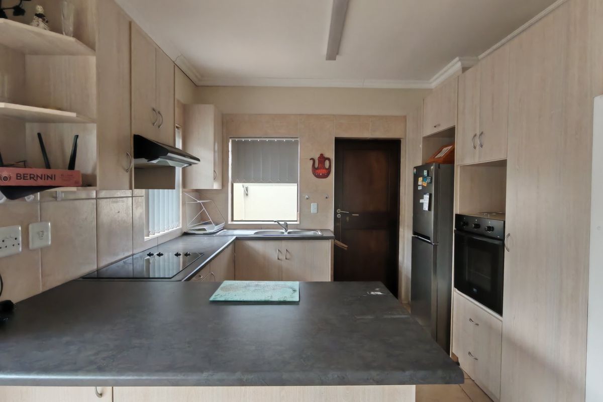 A functional kitchen featuring light-toned laminate cabinetry, dark countertops, built-in oven, electric hob, and a tiled backsplash with direct access to an exterior door.