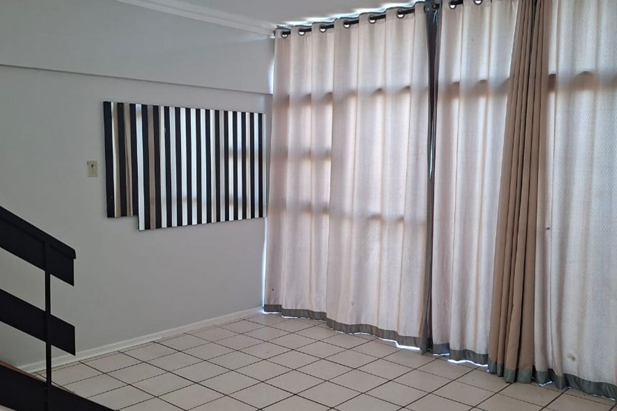 An empty living area featuring tiled flooring, a staircase, and large windows with floor-to-ceiling curtains.