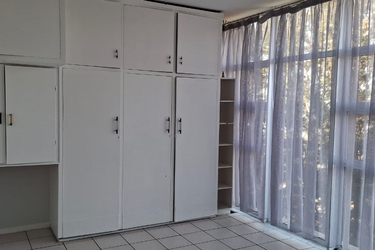 A bright bedroom featuring extensive built-in storage cupboards, tiled flooring, and large windows that provide ample natural light.