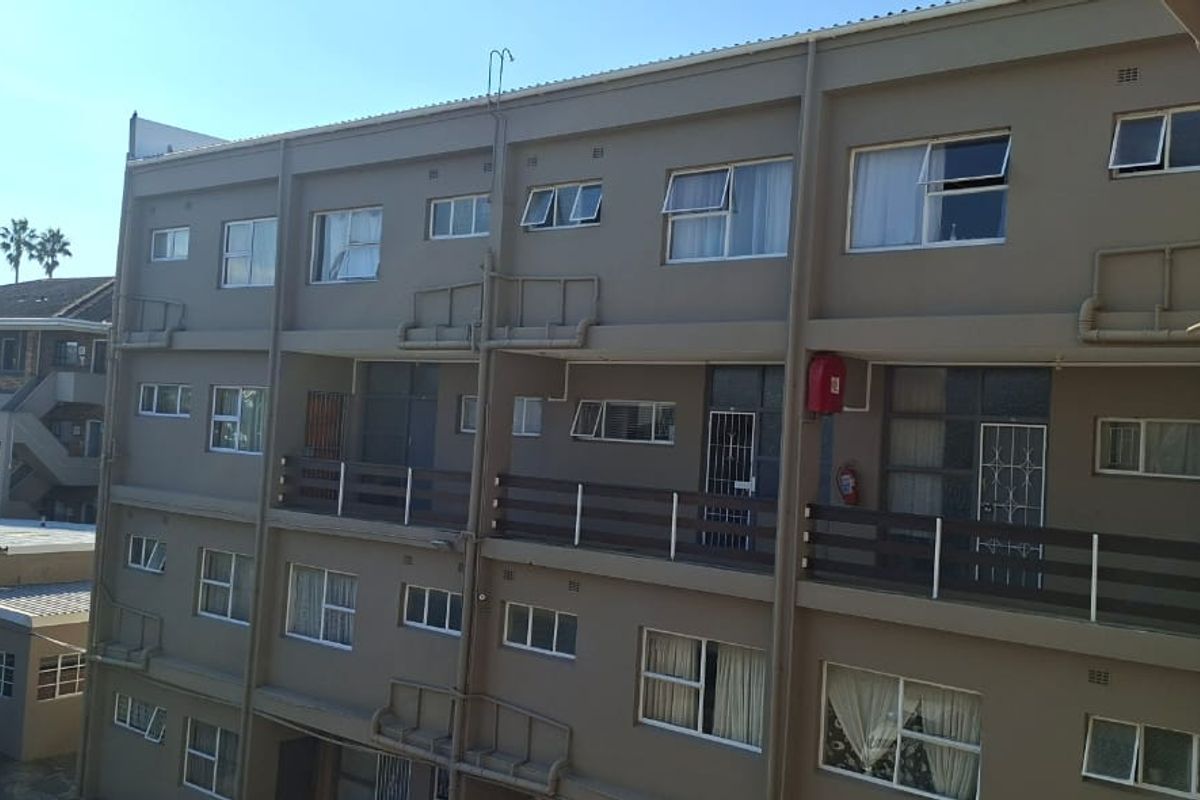 Exterior view of a multi-story apartment building featuring balconies, security gates, and functional exterior infrastructure.