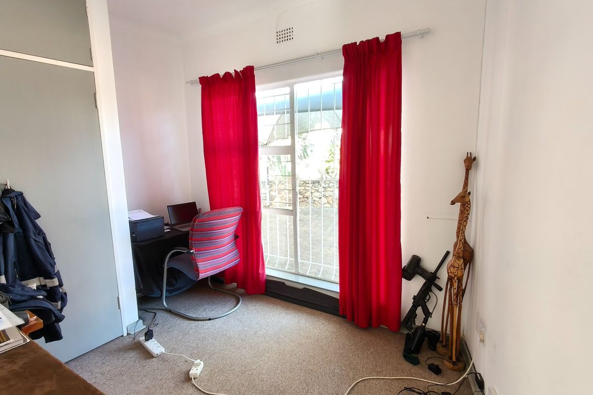 A functional bedroom featuring built-in cupboards, carpeted flooring, and a window fitted with a security gate.