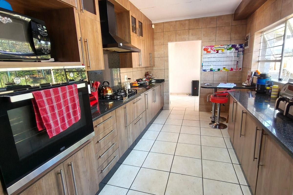 A functional kitchen featuring wood-finish cabinetry, granite countertops, a built-in oven, gas hob, and tiled flooring with a breakfast nook area.