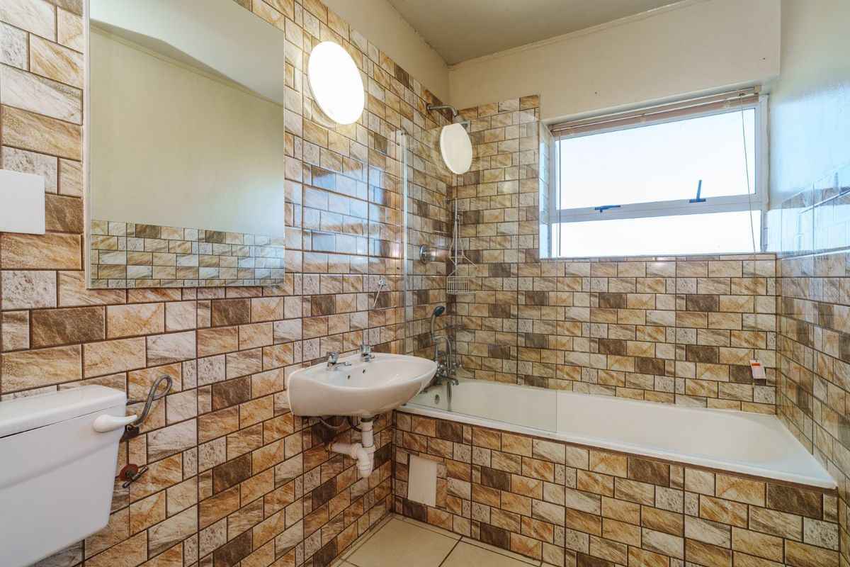 A functional bathroom featuring a bathtub with shower mixer, glass screen, wall-mounted basin, and full-height decorative ceramic wall tiling.