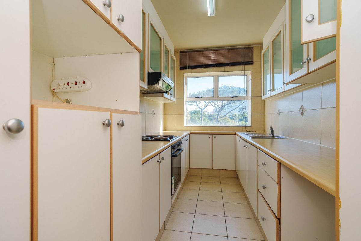 A functional galley-style kitchen featuring built-in cabinetry, laminate countertops, a built-in oven with hob, and tiled flooring with a window providing natural light.