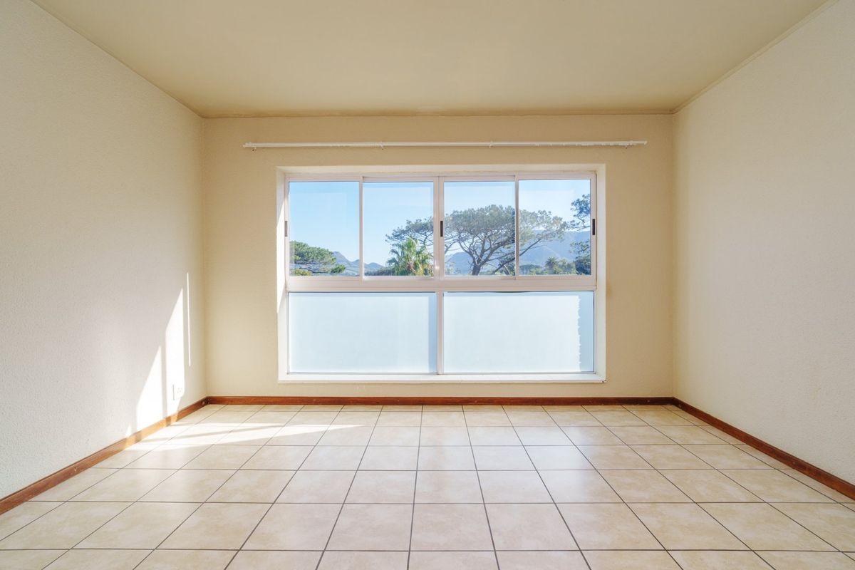 A bright, empty bedroom featuring neutral tiled flooring and a large sliding window with views of the surrounding landscape.