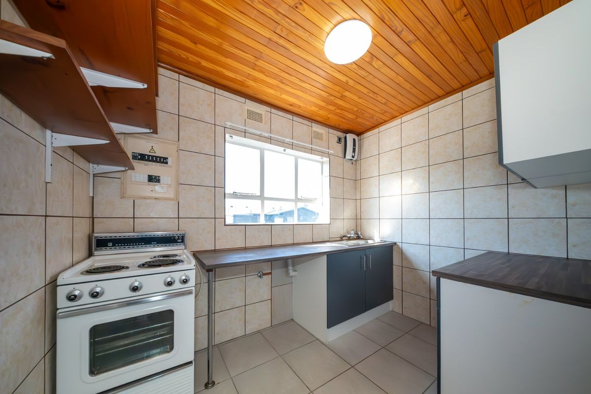 A functional kitchen featuring a freestanding electric stove, tiled backsplash, laminate countertops, and a distinctive timber-clad ceiling.