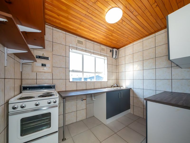 A functional kitchen featuring a freestanding electric stove, tiled backsplash, laminate countertops, and a distinctive timber-clad ceiling.