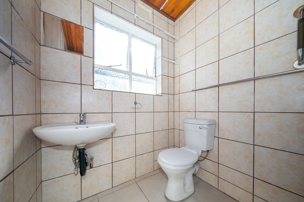 A functional bathroom featuring tiled walls and flooring, a wall-mounted basin, and a standard toilet with a timber ceiling finish.