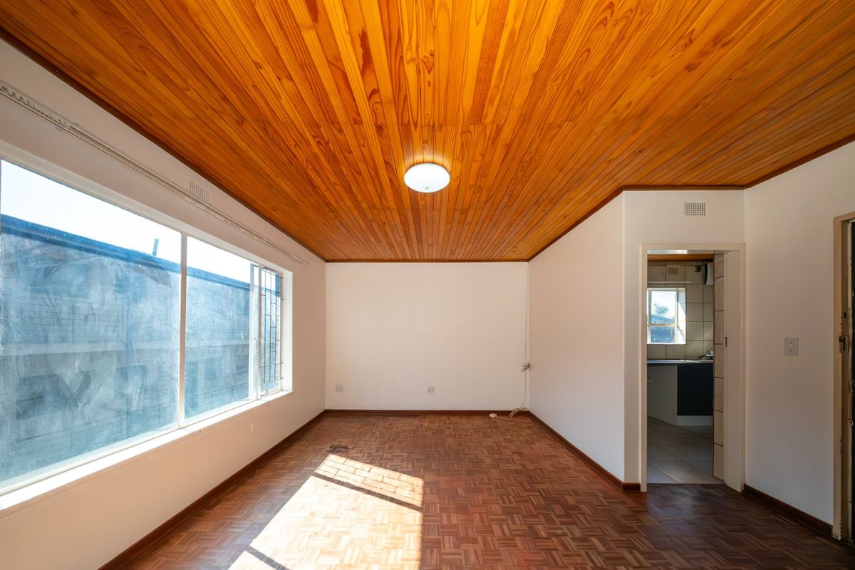 An empty living room featuring classic parquet flooring and a warm timber-paneled ceiling, offering a bright and versatile space for personalization.