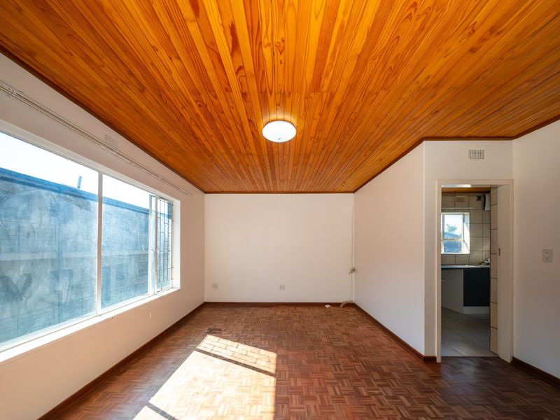 An empty living room featuring classic parquet flooring and a warm timber-paneled ceiling, offering a bright and versatile space for personalization.