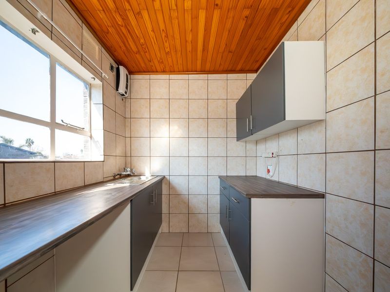 A functional kitchen featuring laminate countertops, built-in cabinetry, a stainless steel sink, and tiled finishes with a timber ceiling.