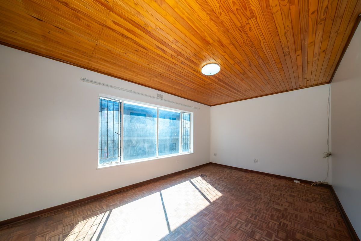 An empty bedroom featuring classic parquet flooring and a warm timber tongue and groove ceiling, providing a neutral canvas for interior design.
