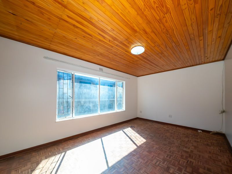 An empty bedroom featuring classic parquet flooring and a warm timber tongue and groove ceiling, providing a neutral canvas for interior design.