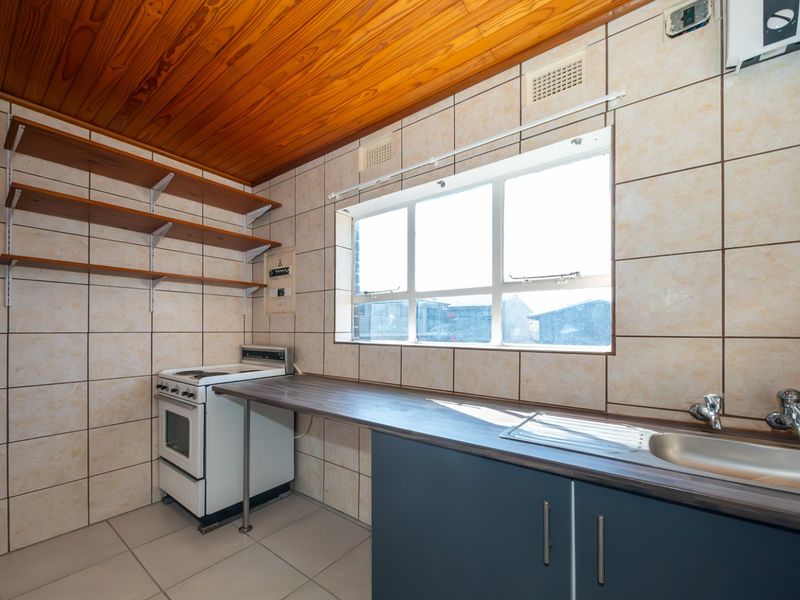 A functional kitchen featuring tiled walls, timber ceiling, stainless steel sink, laminate countertop, and a freestanding stove.