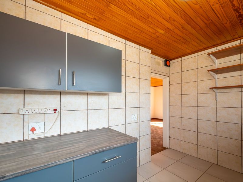 A functional kitchen area featuring modern grey cabinetry, laminate countertops, tiled walls, and a timber-clad ceiling, offering a clean and practical workspace.
